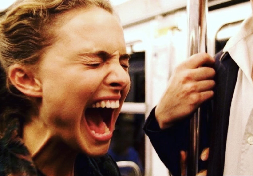 Colour photograph of a woman in profile with her eyes closed in an underground train carriage