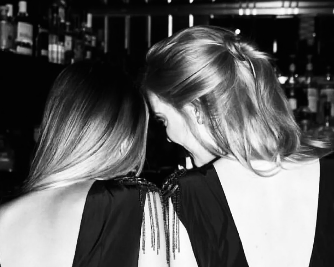 Two women in black evening dresses with elegant ball hairstyles, seen from behind
